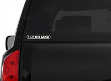 A white "Fish The Land" logo with black inside on the back of a windshield.